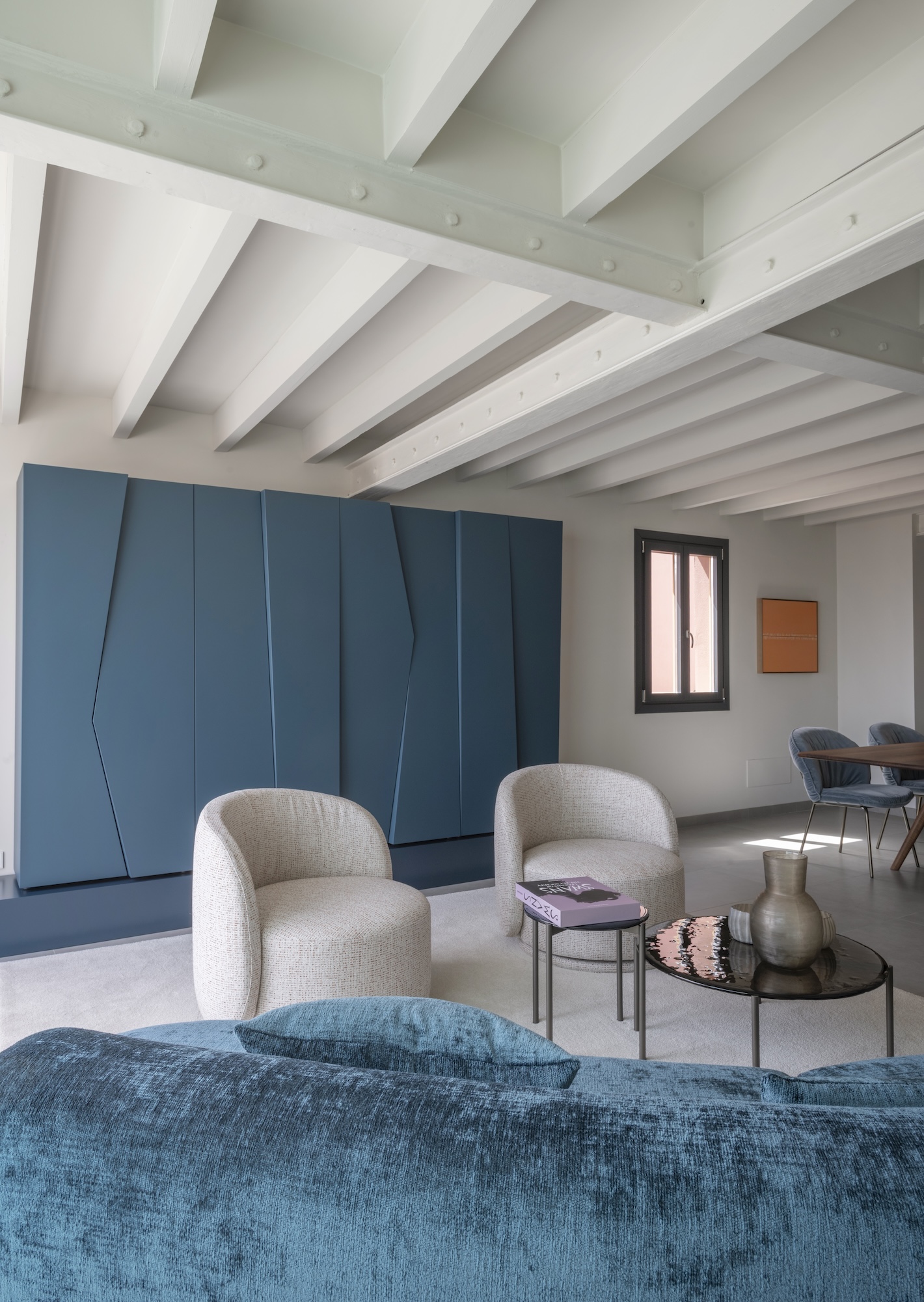 Modernes Wohnzimmer mit blauen und beigen Sesseln, Sofa, schwarzem Couchtisch und dekorativen Elementen.